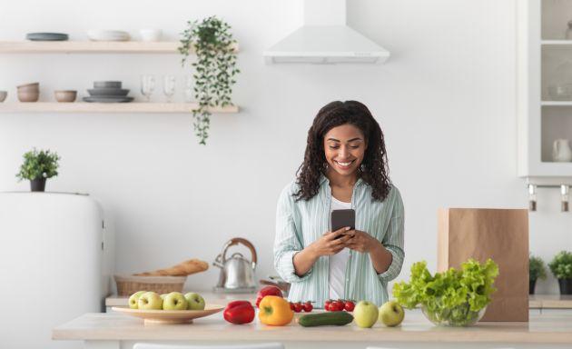 Woman in kitchen looking at phone surrounded by food